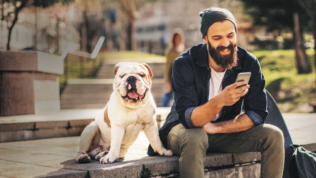 A man sitting with his dog happily checking his mobile banking app.