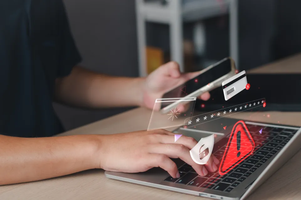 Person typing on computer and phone. Overlay of 3D cyber security illustrations.