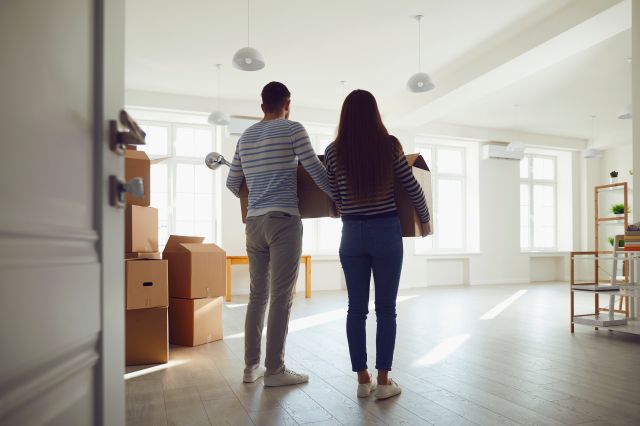 A couple walking into an empty home with boxes in hand.