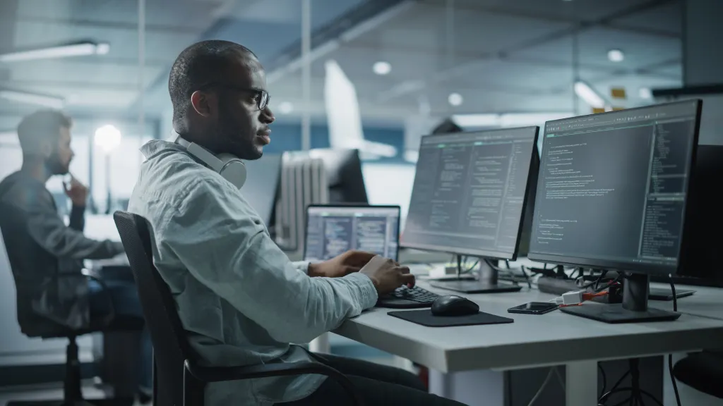 A business leader sits in an office at his desk looking at monitor screens