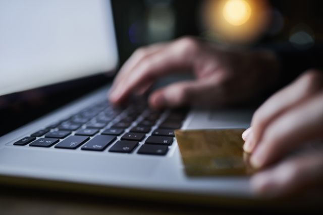 Hand typing on a computer while the other hand holds a credit card.