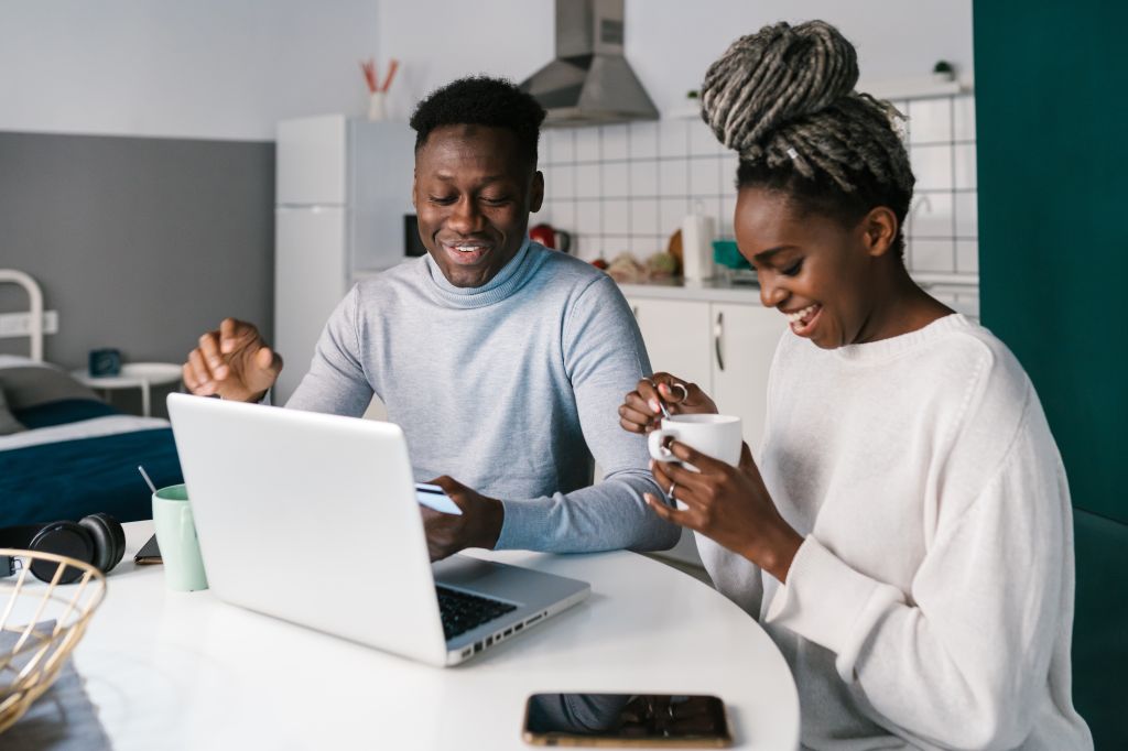 Happy young couple using a laptop and credit card in their first home
