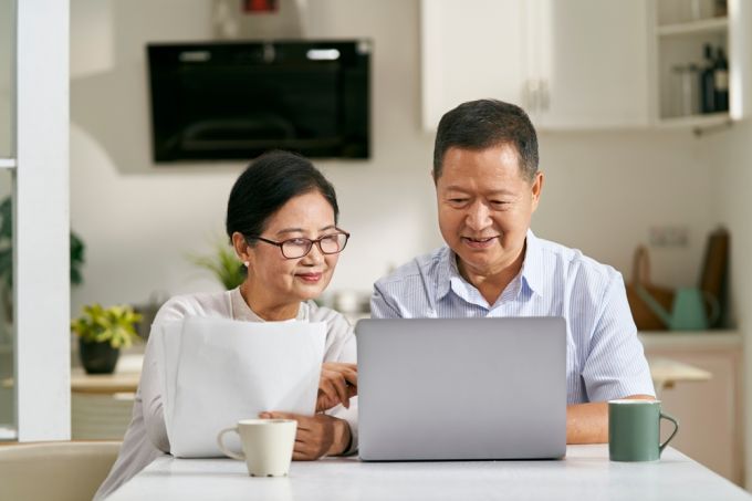 Elderly couple sitting on a couch while browsing on a computer.