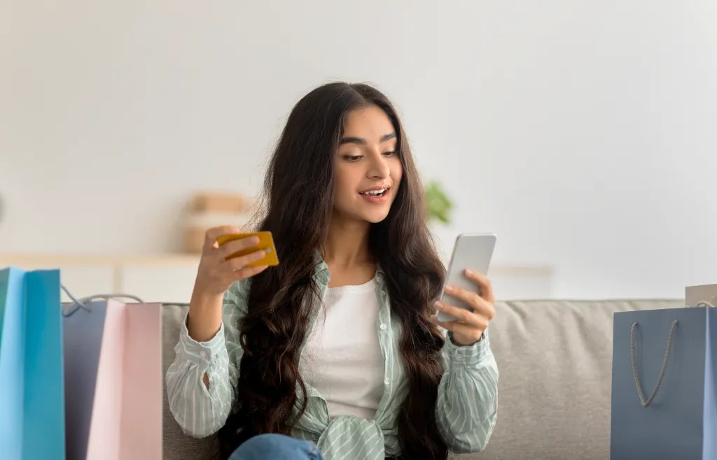 Young woman sitting on a couch with a credit card in one hand and a smartphone in the other, reviewing a Buy Now Pay Later payment option for a purchase.
