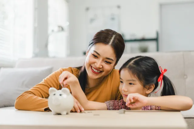 Mother and daughter talking about money with the daughter putting coins into a piggybank