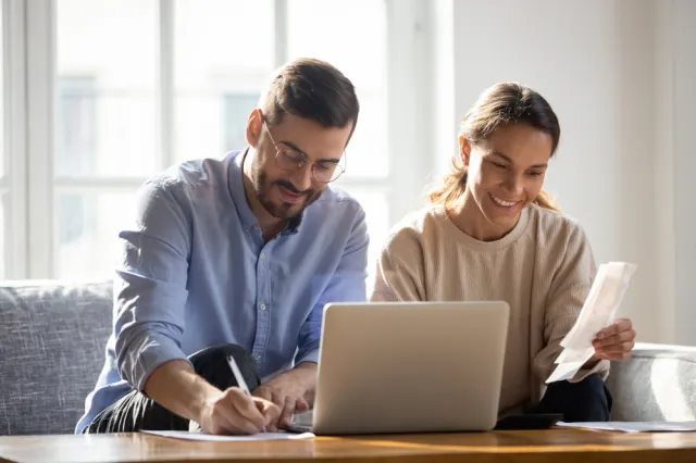 A man and a woman sitting in front of a computer and reviewing receipts.