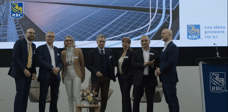 Six business professionals standing on stage at an RBC corporate event with solar panel imagery displayed on screen behind them