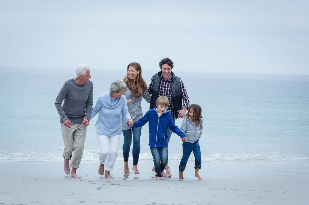 Three generations of a family on a beach representing the sandwich generation who care for elderly parents while raising children.