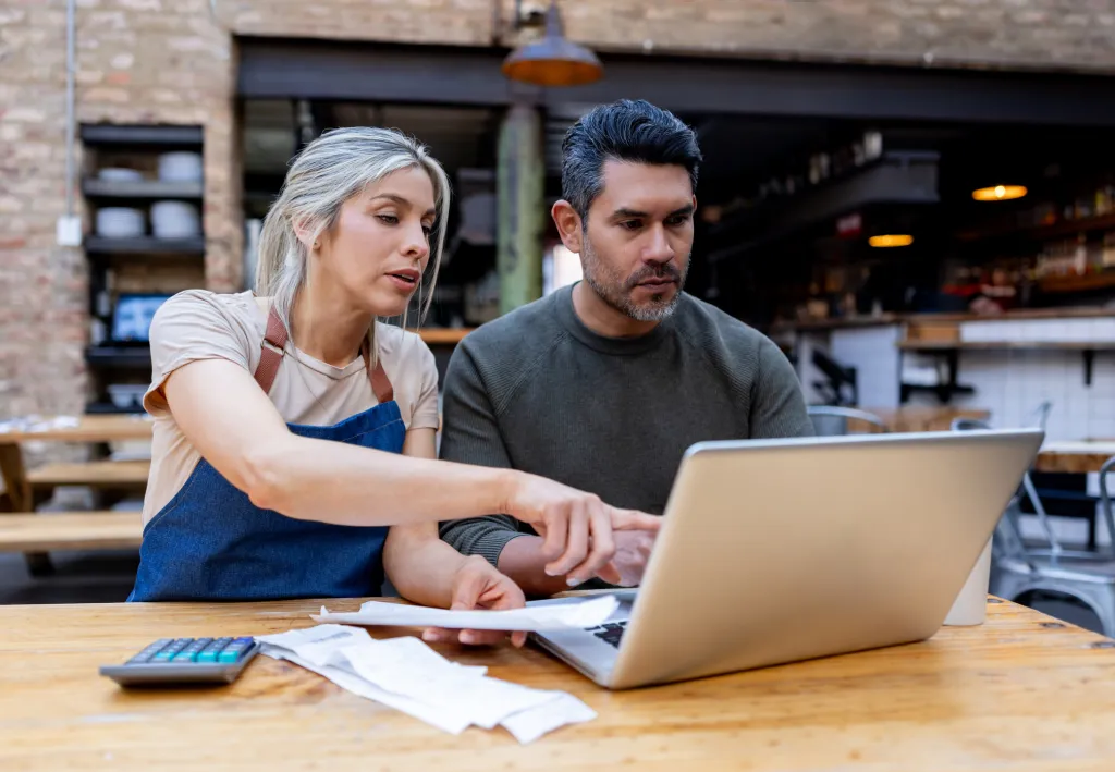 Business owners reviewing financial documents on laptop with calculator