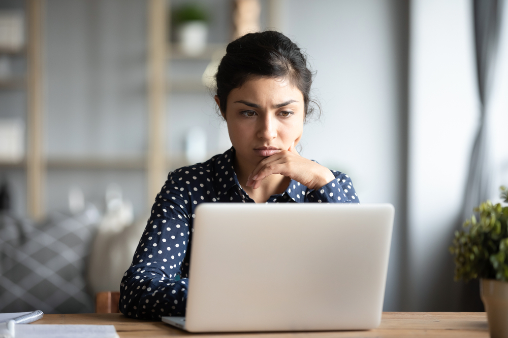 Young woman sitting on a couch with a computer on her lap and a phone in her hands.