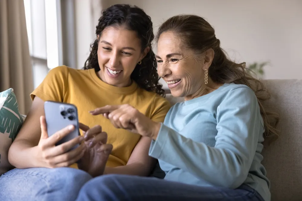 Young woman and elderly woman sitting together while browsing on a phone.