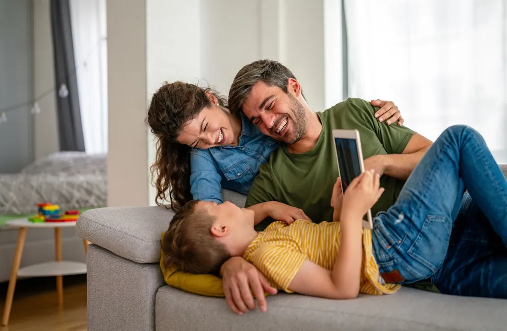 Parents reviewing online safety habits with their child as he plays on a tablet.
