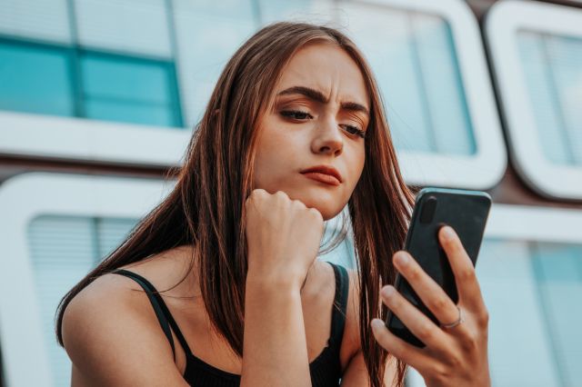 Woman looking at phone with confused expression.