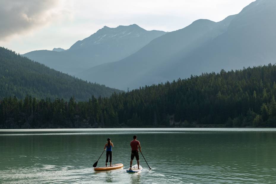 Deux personnes naviguent en planche à pagaie sur un lac entouré de paysages de montagne.