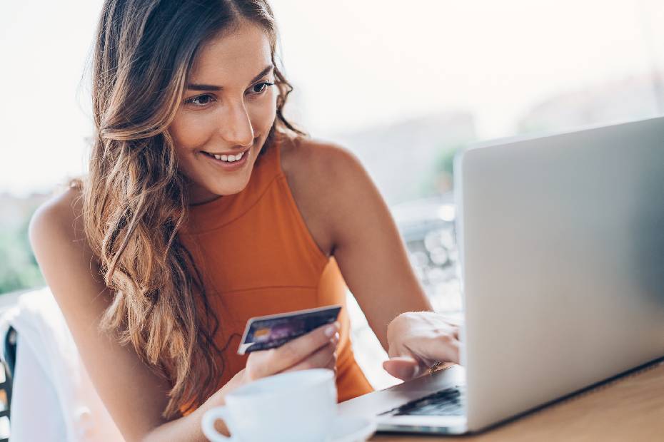 Une jeune femme utilisant une application de paiement P2P sur son ordinateur, tenant une carte de crédit