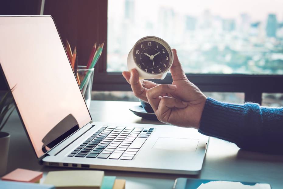 Tenant à la main une petite horloge à côté d'un ordinateur portable ouvert.