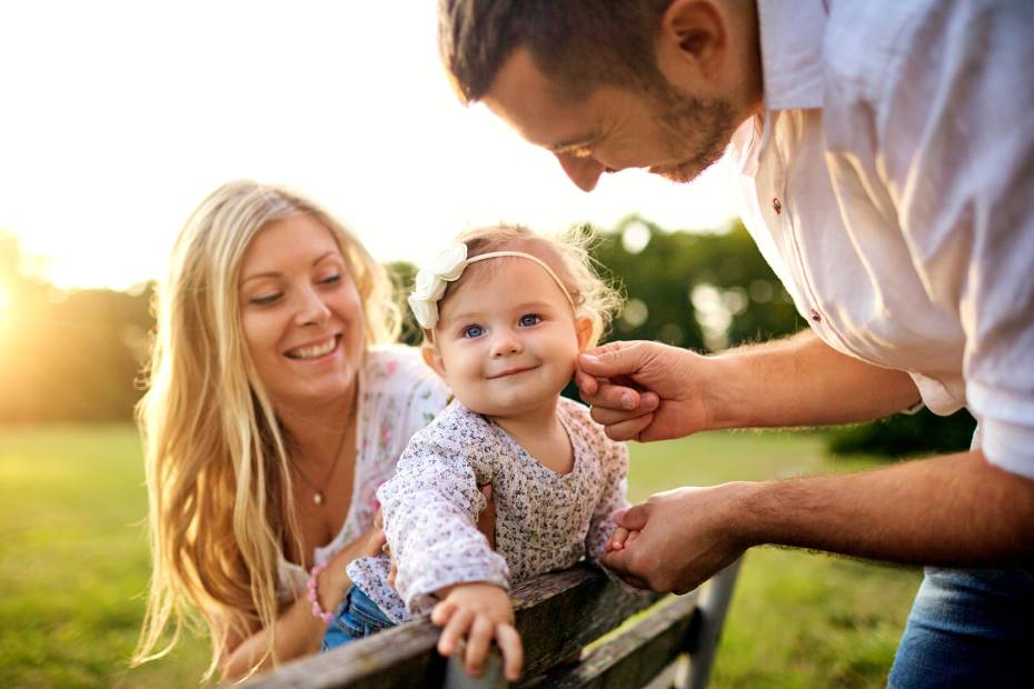 Image d'une jeune famille heureuse installée sur un banc de parc ; le père caresse le visage de la petite fille que tient la mère.