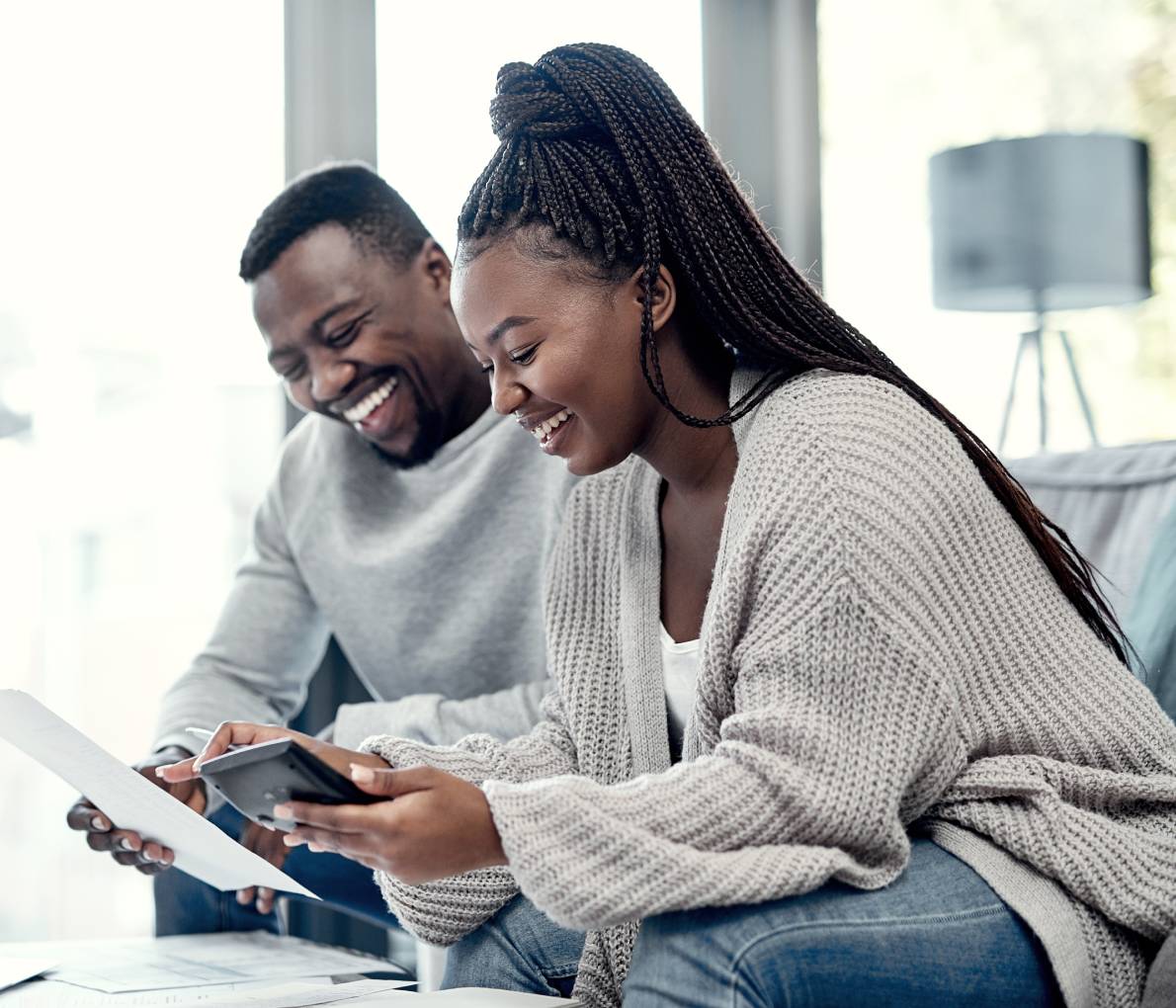 Un couple noir souriant assis sur un canapé blanc, examinant les options de paiement hypothécaire sur une tablette