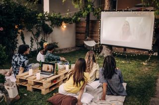 Groupe d'amis regardant un film sur projecteur dans un jardin.