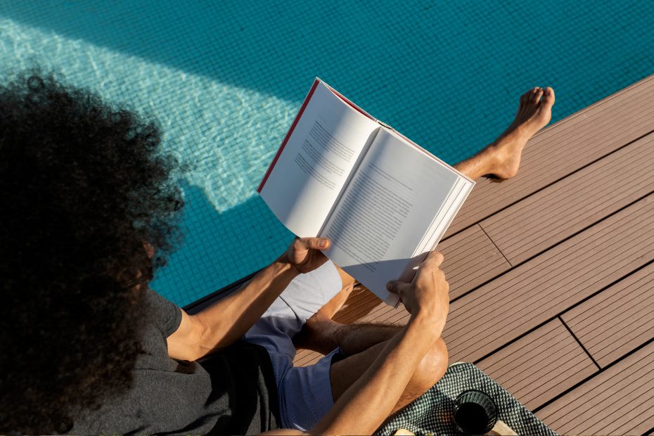 Une personne lisant un livre à côté d'une piscine.