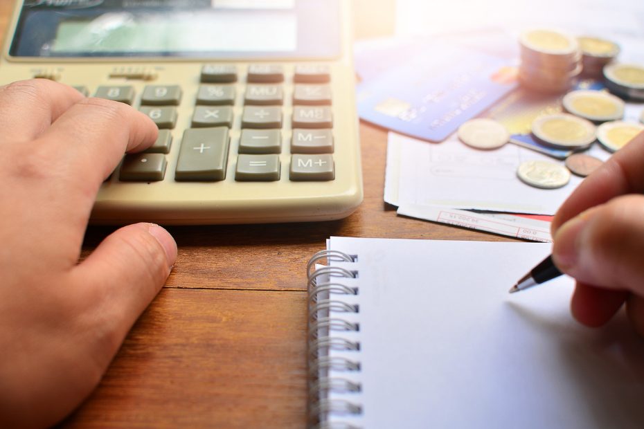 Une main posée sur une calculatrice, sur fond flou de cartes de crédit et de pièces de monnaie