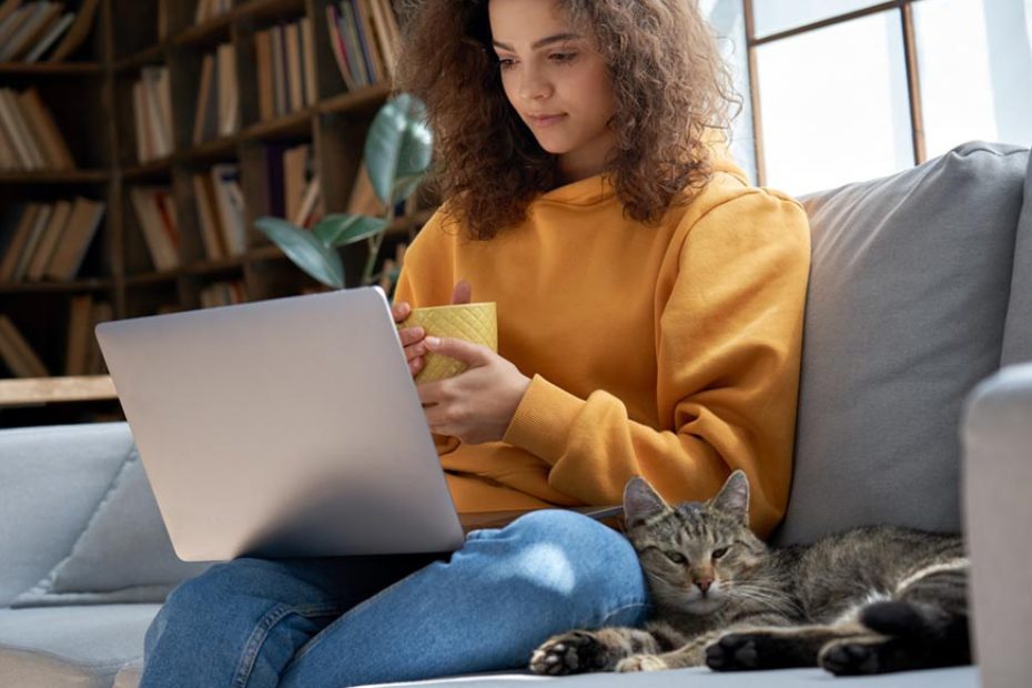 Une femme assise sur un canapé regarde son ordinateur portable.