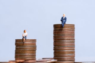Représentation de l'écart de richesse : figurines d'une femme sur un petit tas de pièces et d'un vieil homme bien habillé sur une pile plus haute