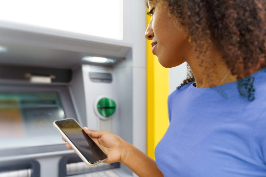 Une jeune femme noire effectue des opérations bancaires au guichet automatique.