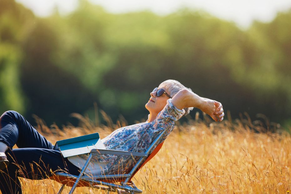 Femme se relaxant avec un livre dans un champ ensoleillé.