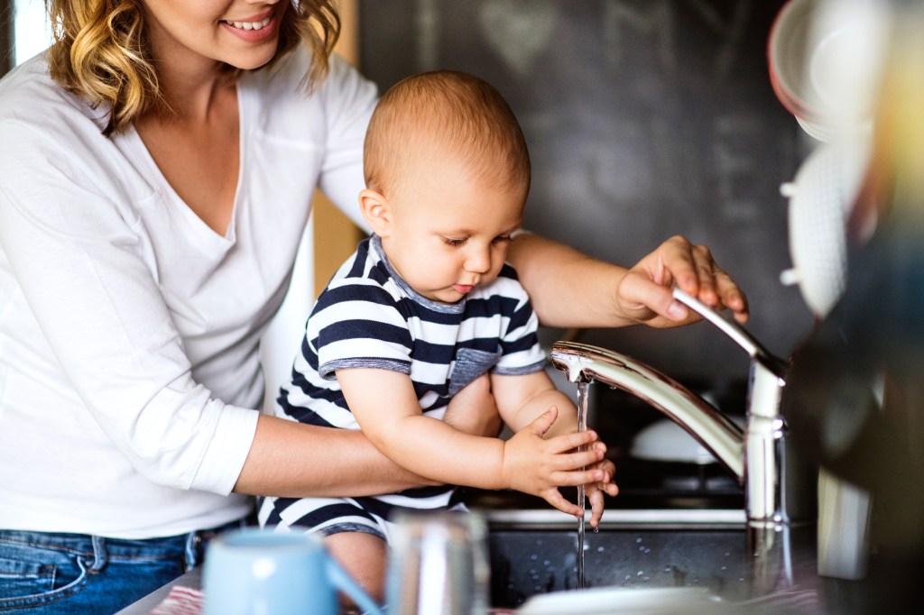 Parent tenant un jeune enfant qui se lave les mains sous le robinet de la cuisine.