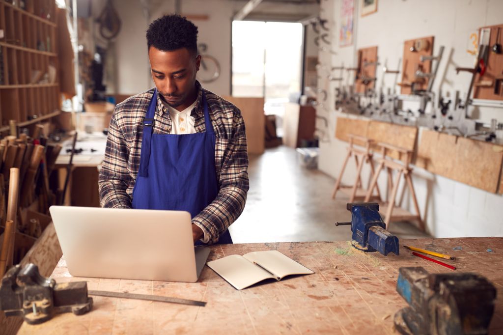 Artisan masculin dans un atelier de menuiserie pour vélos en bambou faisant des comptes sur un ordinateur portable