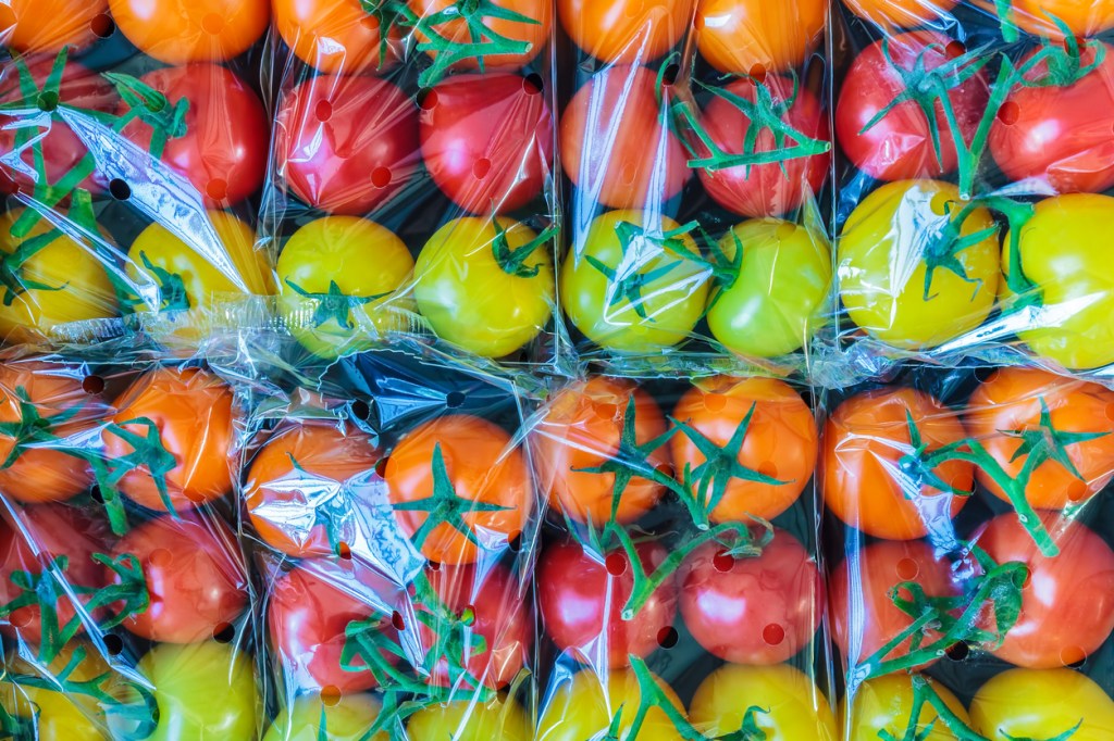 Affichage de tomates cerises jaunes, oranges et rouges emballées dans du plastique frais