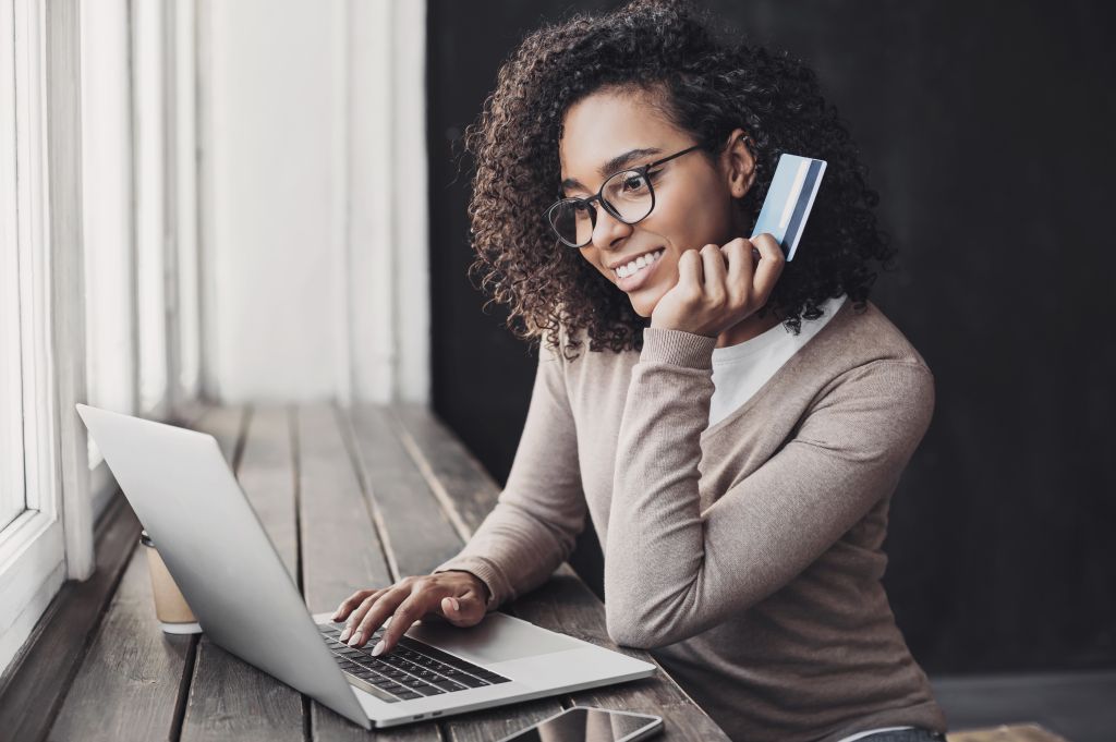 Jeune femme tenant une carte de crédit et utilisant un ordinateur portable pour effectuer le paiement