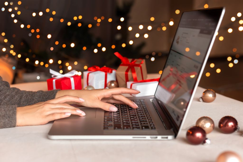 les mains d'une femme tapant sur un ordinateur portable avec des cadeaux emballés