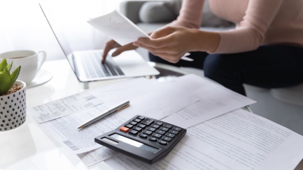 une femme assise à une table examine ses factures et se sert d’une calculatrice