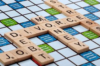 Une planche de Scrabble sur laquelle sont épelés en anglais les mots « divorce », « dette » et « argent »