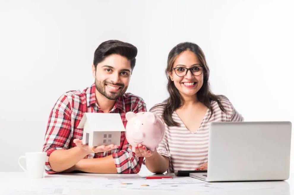 Jeune couple heureux tenant une maison miniature et une tirelire.