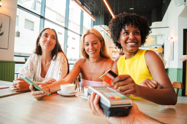 3 femmes savourant un café dans un café tout en payant avec leur carte de crédit