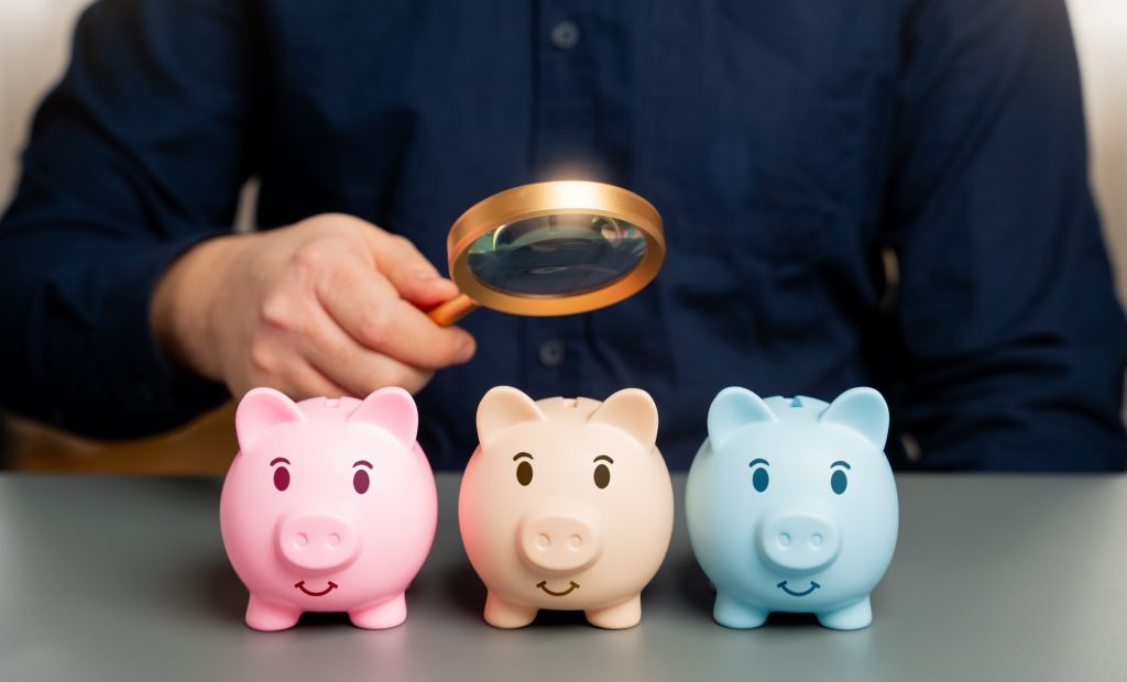 Magnifying glass looking over piggy banks.