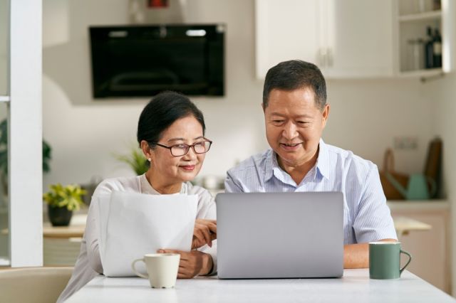 Elderly couple sitting on a couch while browsing on a computer.
