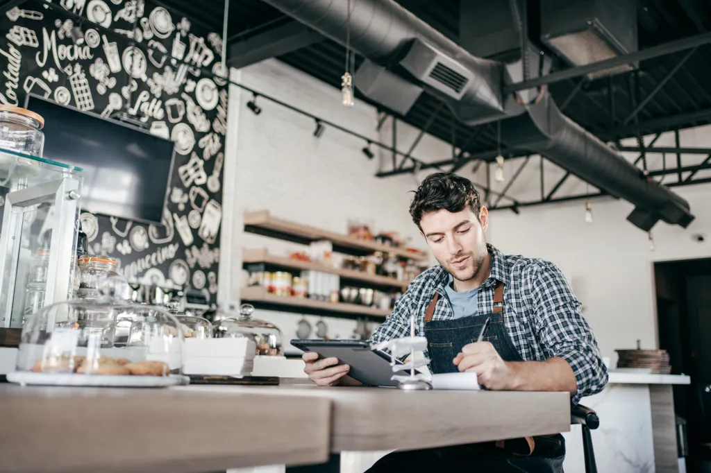 Image d’un homme dans un café tenant une tablette d’une main et prenant des notes de l’autre