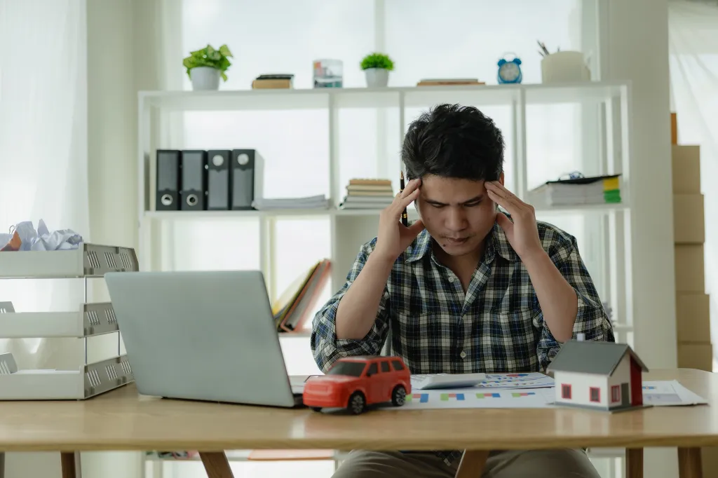 L'homme est stressé par les factures, les paiements automobiles, les paiements hypothécaires, et se tient la tête entre les mains en regardant les factures. Confus à propos des informations financières ou préoccupé par les dépenses et la budgétisation.