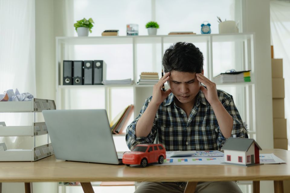 L'homme est stressé par les factures, les paiements automobiles, les paiements hypothécaires, et se tient la tête entre les mains en regardant les factures. Confus à propos des informations financières ou préoccupé par les dépenses et la budgétisation.