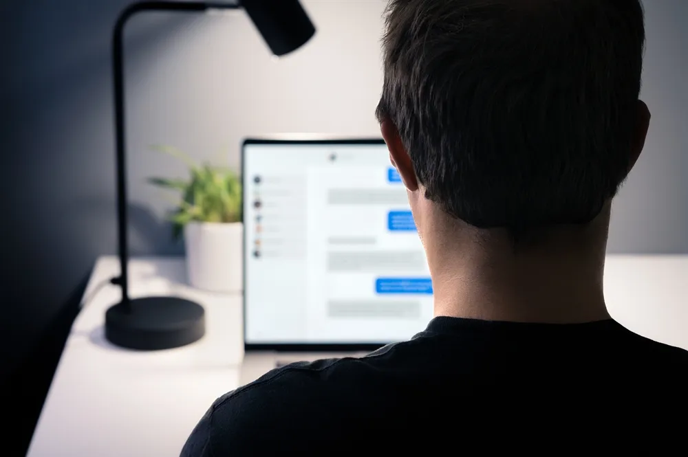 Man sitting at a desk while messaging on a computer.