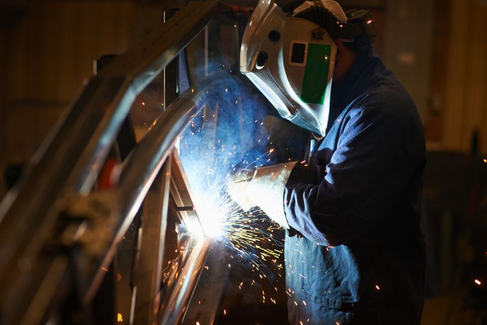 Homme en salopette bleue et écran de protection effectuant une soudure à l'arc dans un environnement industriel