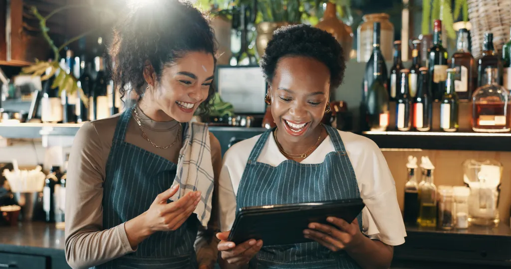 Deux propriétaires de petites entreprises souriants souriants souriants à une tablette tout en examinant la demande financière ensemble derrière un comptoir caf é.