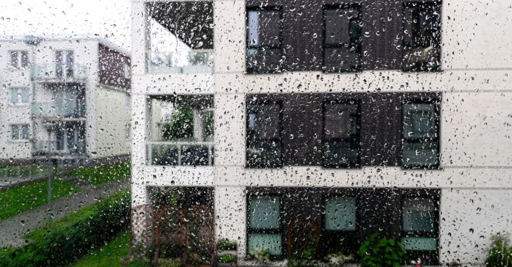 Gouttes de pluie sur la vitre d'une fenêtre avec vue sur des immeubles d'appartements.