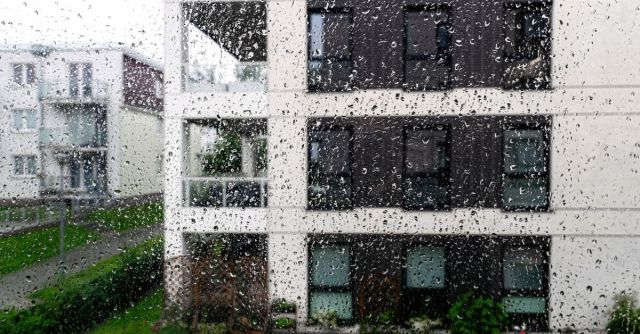 Gouttes de pluie sur la vitre d'une fenêtre avec vue sur des immeubles d'appartements.