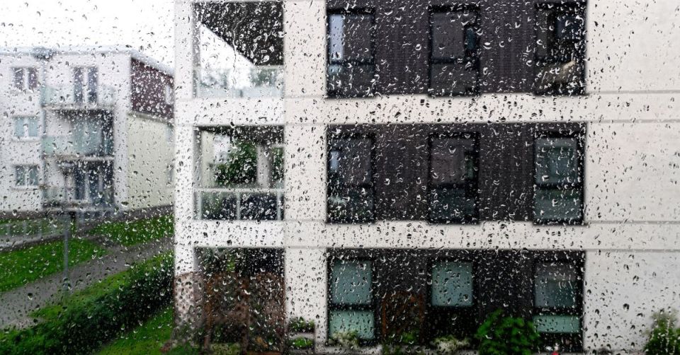 Gouttes de pluie sur la vitre d'une fenêtre avec vue sur des immeubles d'appartements.