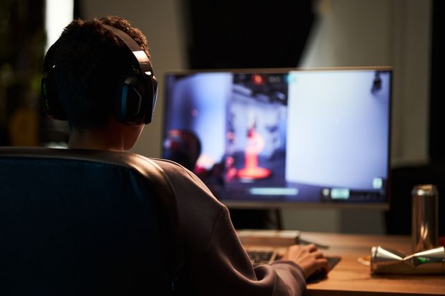 Teenage boy participating in an online game while sitting at his desk.
